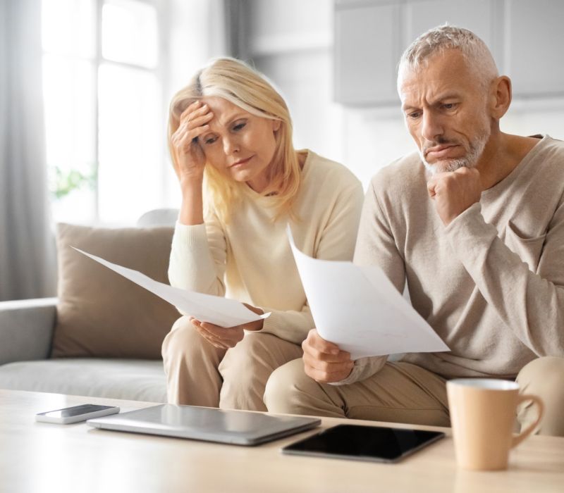 Ein besorgtes Paar sitzt an einem Tisch mit ausgebreiteten Rechnungen und Dokummenten und überprüft seine Finanzen